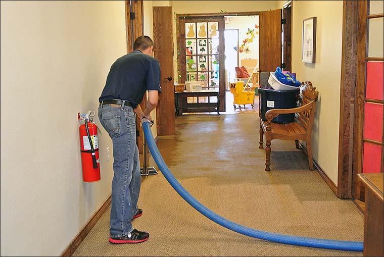 Restoration technician extracting water from carpet at a commercial property