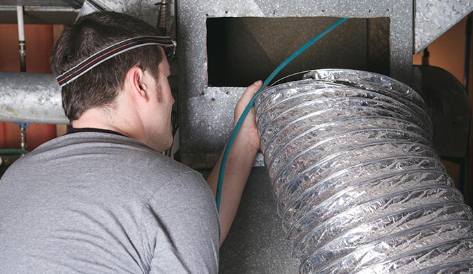 Technician inspecting and cleaning an HVAC duct system for maintenance