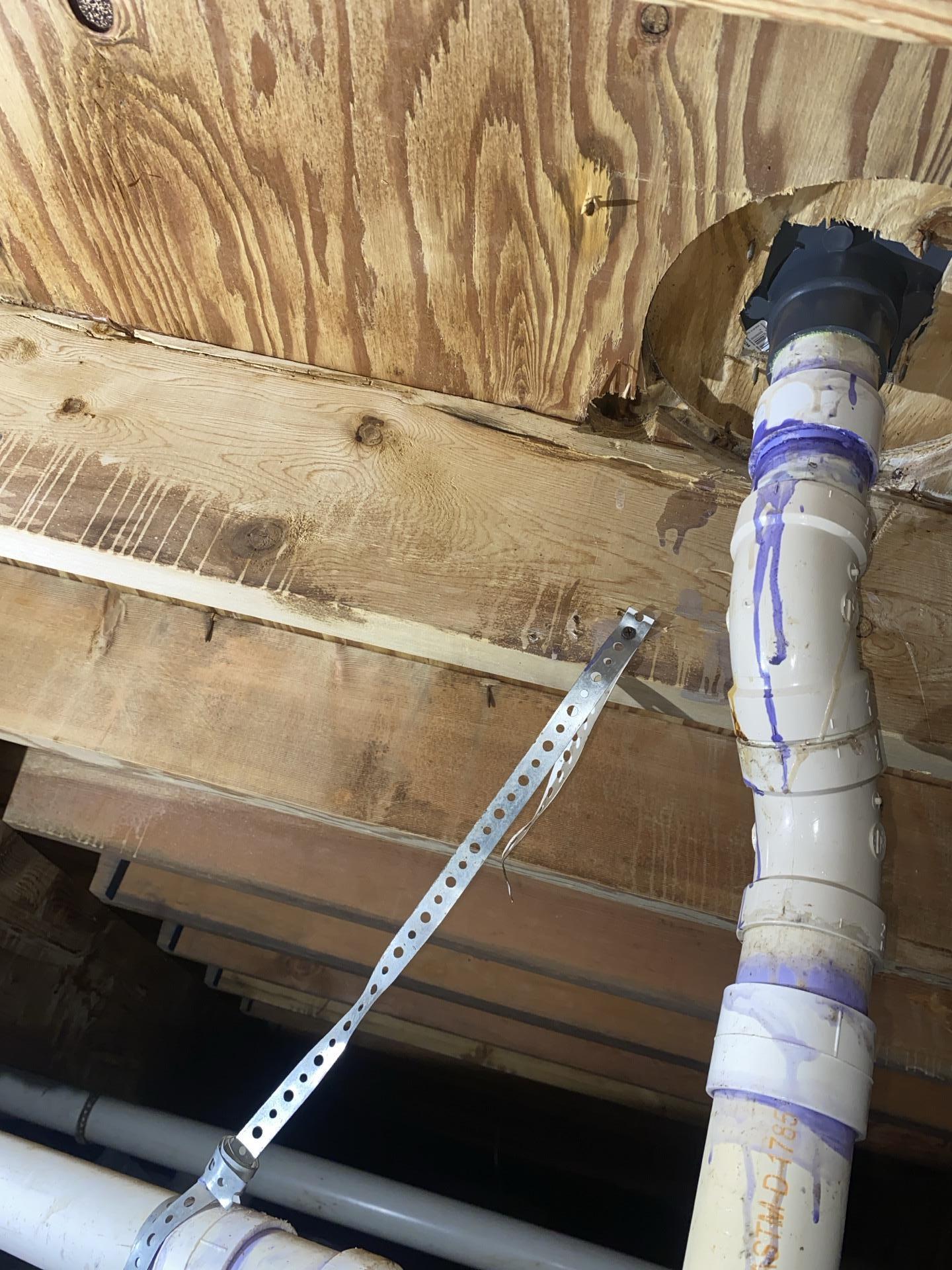 View from a crawlspace showing PVC plumbing pipes and the underside of a wooden subfloor with signs of past water exposure.