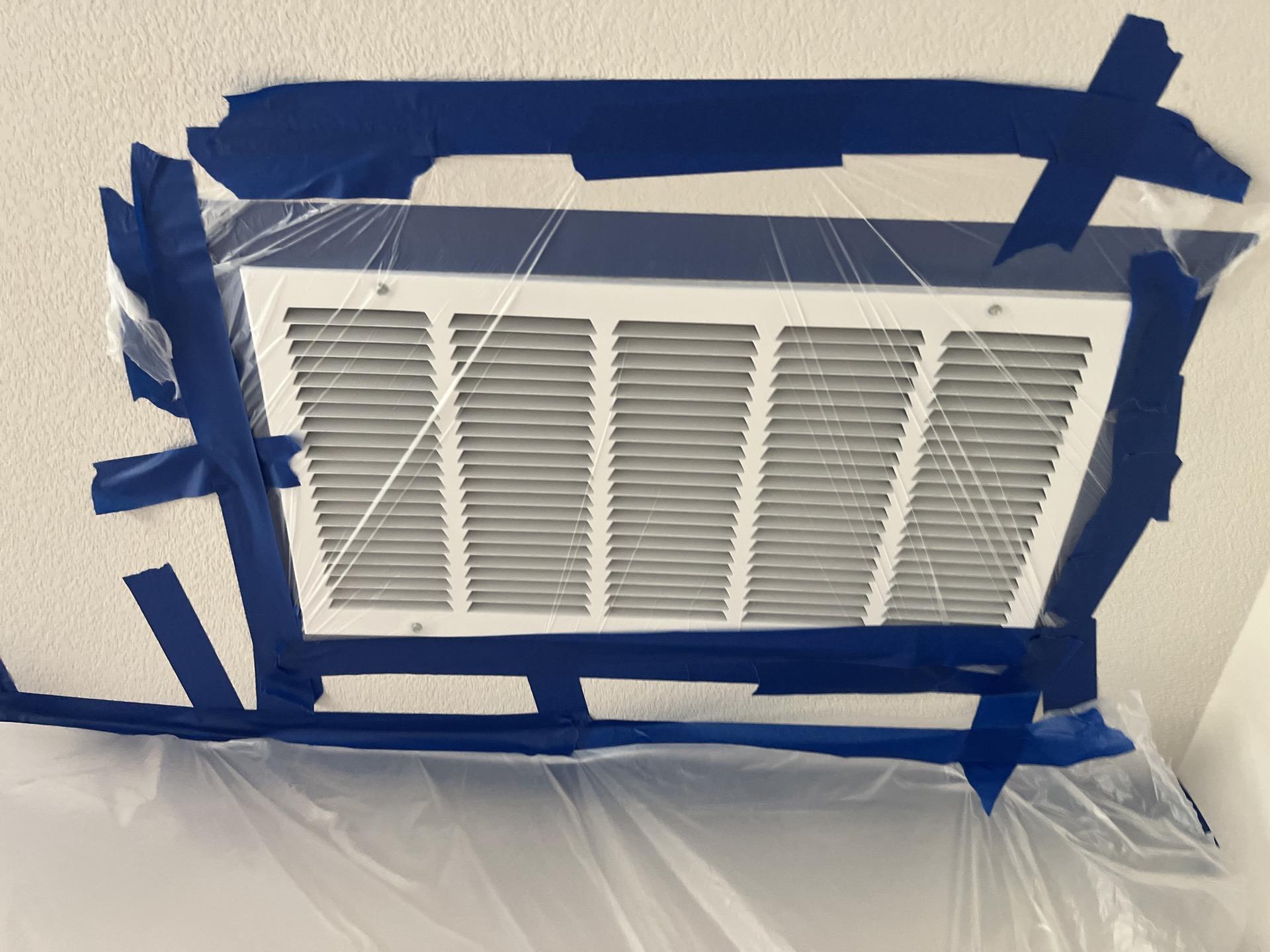 Overhead HVAC air register sealed with plastic and tape to protect the ventilation system during restoration.
