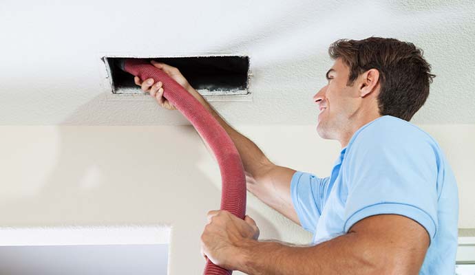 Technician cleaning air duct vent in ceiling