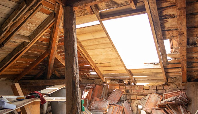 Attic under renovation with exposed wooden roof beams, large roof opening, and old roof tiles on the floor